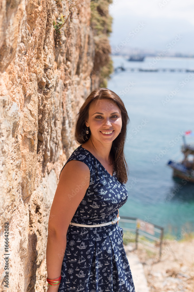 Young woman standing near old stone wall with sea on backgorund Young woman standing near old stone wall with sea on backgorund