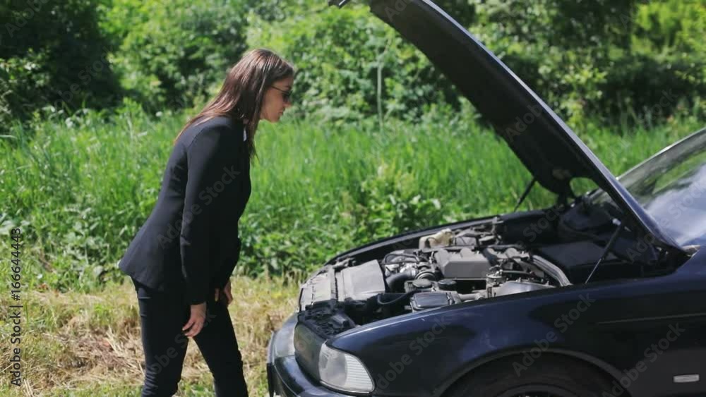 A woman waits for assistance with her car broke down on the road side, after calling for help, using smartphone A woman waits for assistance with her car broke down on the road side, after calling for help, using smartphone