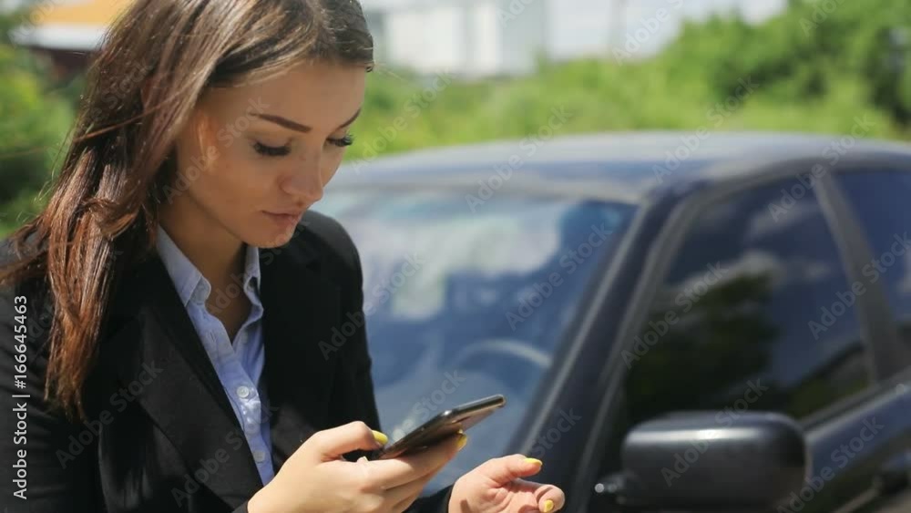 Elegant beautiful model girl sitting on hood of her car, using smartphone phablet, countryside background, sun shining, summer day Elegant beautiful model girl sitting on hood of her car, using smartphone phablet, countryside background, sun shining, summer day