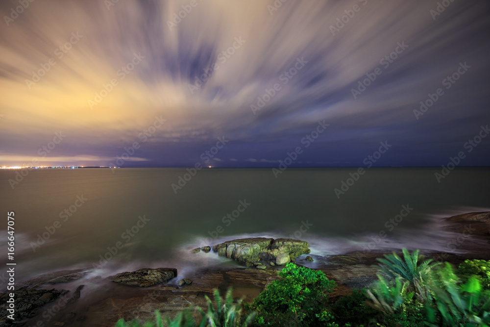 Long exposure photography of the ocean in the evening. Romantic atmosphere of peaceful night at sea. Big rocks near smooth shoreline.