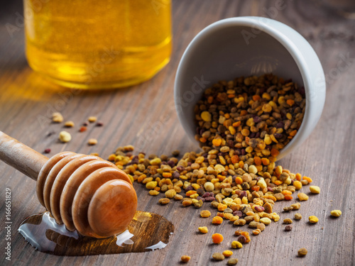 Closeup view of bee pollen and honey dipper with honey on brown wooden table