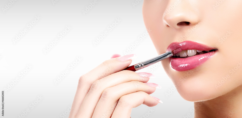 Closeup shot of woman's lips and hand holding a makeup brush against a grey background with copyspace