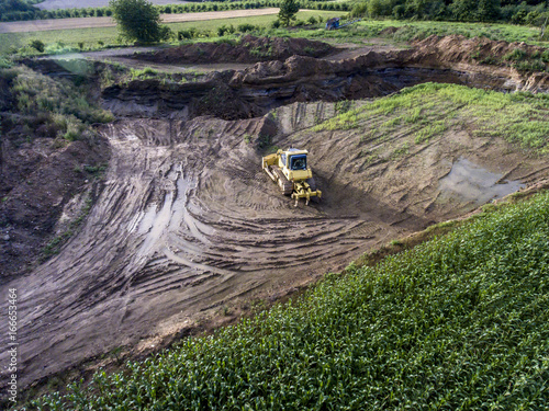 top view heavy machine excavator bagger working in mud on construction site with green landscape surrounding