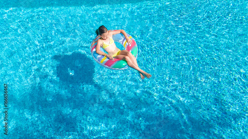 Aerial view of girl in swimming pool from above, kid swim on inflatable ring donut and has fun in water on family vacation 