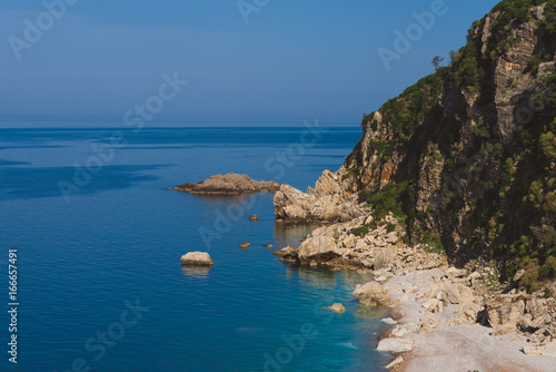 Adriatic sea coast by sunny day summer landscape. Pebble beach, rocks and green tree brunches under blue sky near Perazica Do village on the way to Petrovac, Montenegro. photo