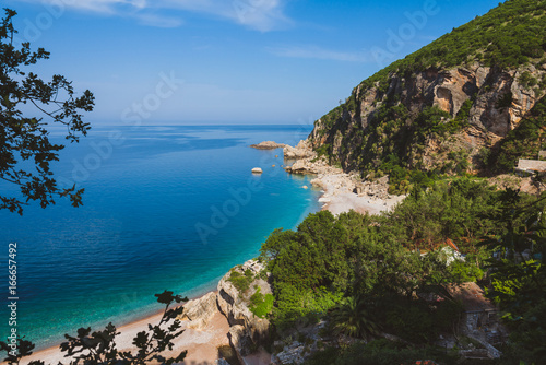 Adriatic sea coast by sunny day summer landscape. Pebble beach, house roofs and green tree brunches under blue sky near Perazica Do village on the way to Petrovac, Montenegro. © krugli