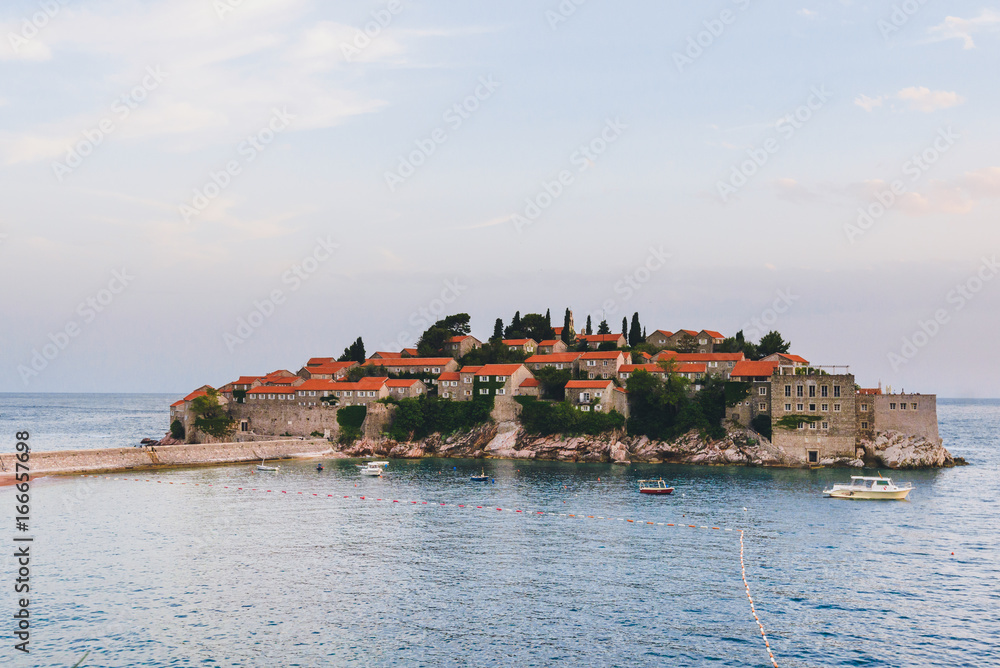 Sveti Stefan island landscape near Budva, Montenegro. Evening view of Adriatic sea, St. Stefan luxury fortificated village and sea boats.