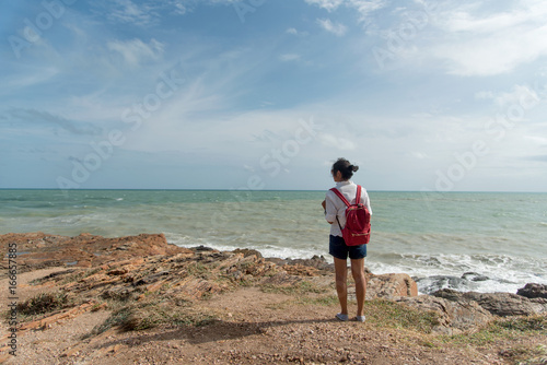 Happy young traveler with a backpack, enjoying the view of a tropical beach on a background the mountains. Young backpacker traveling along Asia, happy female walking discovering world