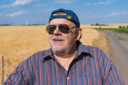 Outdoor portrait of smiling senior farmer standing at the wheat field edge and satisfied with future harvest © Yuri Kravchenko