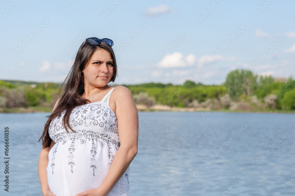 Obraz premium Pregnant woman in a white dress near the water
