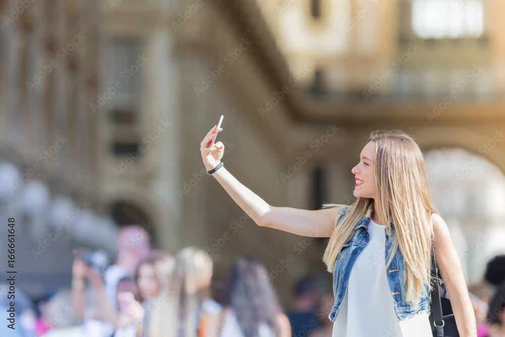 Pretty young tourist taking a selfie with her mobile phone in Milan, Italy