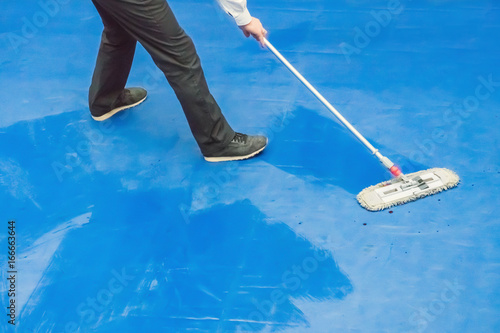 Man wipes a drops of blood from a boxing ring with a mop photo