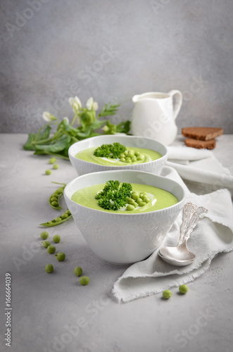 Green pea soup in bowls on grey concrete or stone background, selective focus, copy space