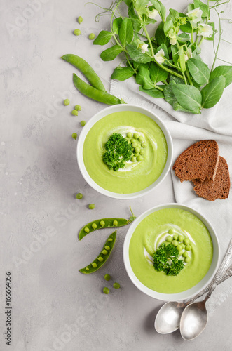 Green pea soup in bowls on grey concrete or stone background, top view, copy space, vertical