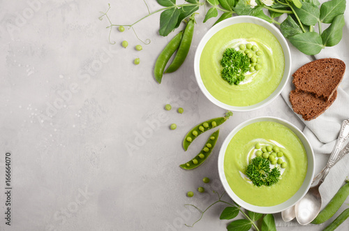 Green pea soup in bowls on grey concrete or stone background, top view, copy space, horizontal