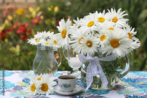 Daisies in a glass jar and candles. Flower decoration in the garden.