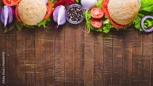 Hamburger with cheese, meat, tomatoes and onions and herbs. On Wooden background. Top view. Free space.