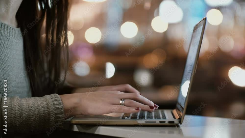 Close-up view of female hands typing on laptop computer. Young woman sitting near the window in evening and use wi-fi. Close-up view of female hands typing on laptop computer. Young woman sitting near the window in evening and use wi-fi.