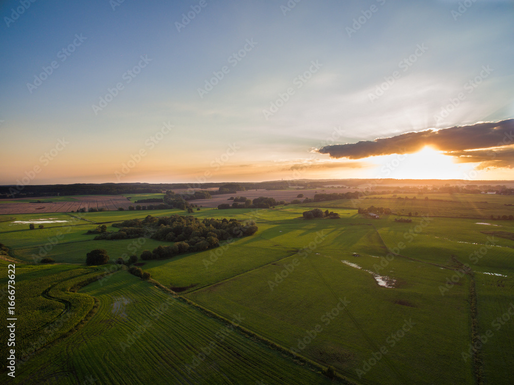 
aerial view of a beautiful sunset with sunbeams above green agricultural fields in the summer