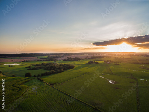  aerial view of a beautiful sunset with sunbeams above green agricultural fields in the summer