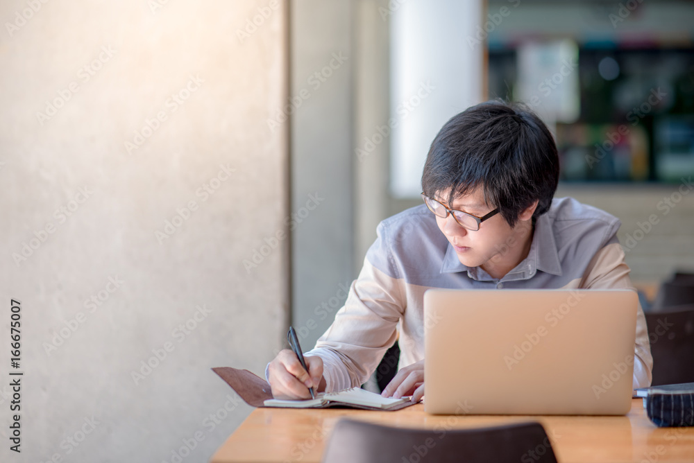 Young Asian man writing on notebook and working with laptop computer in college building. high school or university student, educational concepts Young Asian man writing on notebook and working with laptop computer in college building. high school or university student, educational concepts