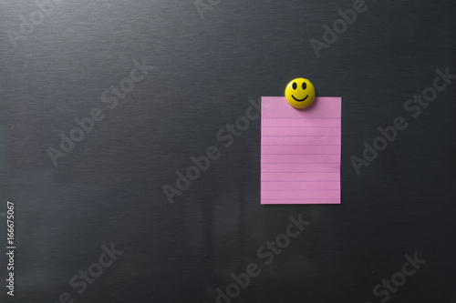 Empty pink paper on refrigerator door with smilling face on magnet.