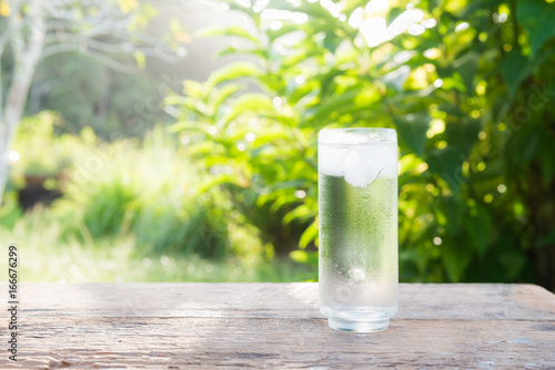 Close up glass of cold water with ice on table with blur garden background