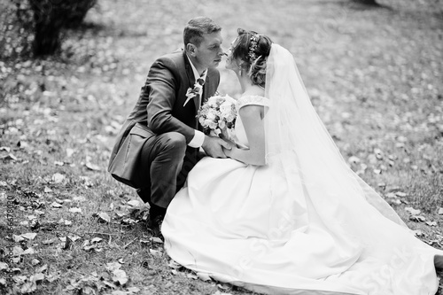 Fabulous young wedding couple sitting on the grass in the park on the sunny day. Black and white photo.