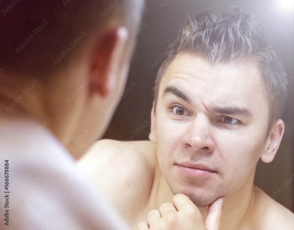 Fototapeta premium The young man looks at himself in the mirror