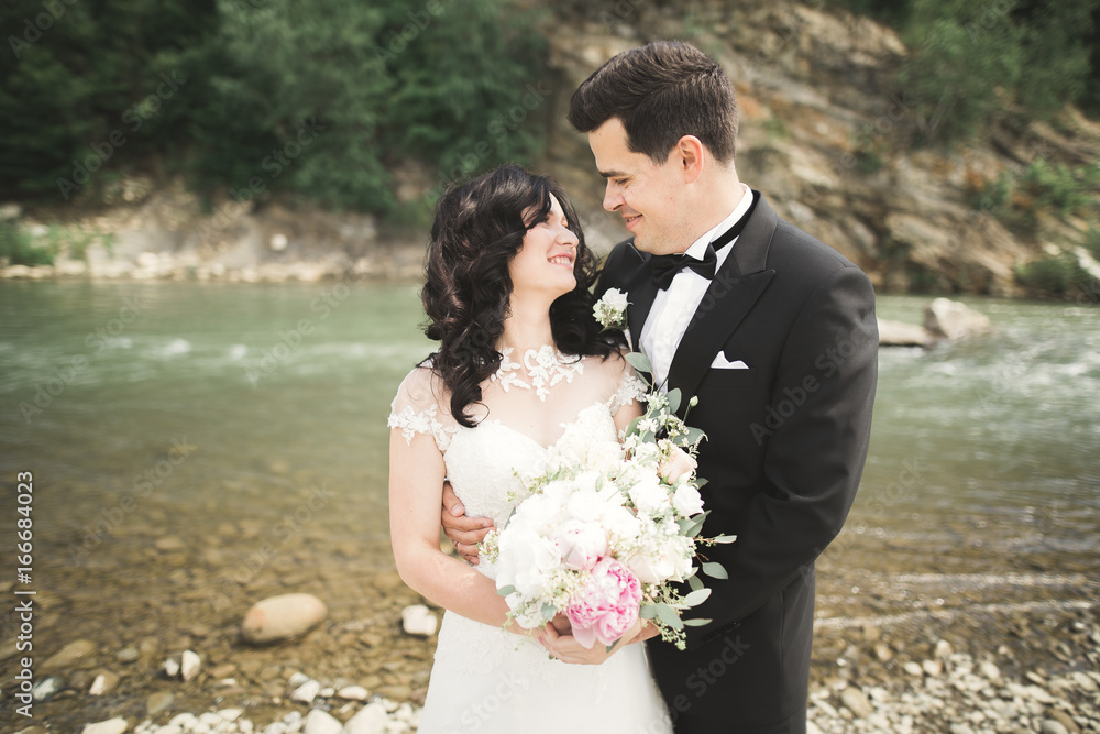 Elegant gentle stylish groom and bride near river with stones. Wedding couple in love Elegant gentle stylish groom and bride near river with stones. Wedding couple in love
