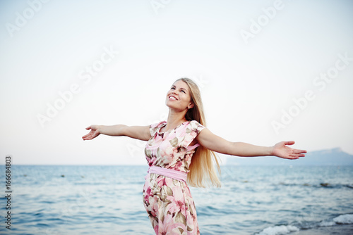 Happy smiling pregnant woman with outstretched arms enjoying sunset on the beach. 