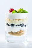 sweet Italian Tiramisu dessert in a glass with raspberries, blueberries, mint and mascarpone on light background