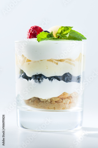 sweet Italian Tiramisu dessert in a glass with raspberries, blueberries, mint and mascarpone on light background