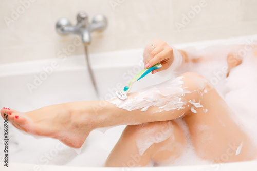 Young woman shaving her legs in bath.