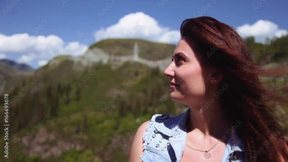 Portrait. A beautiful girl is sitting at a height and admiring the beautiful nature. The wind blows her hair. Slow motion Portrait. A beautiful girl is sitting at a height and admiring the beautiful nature. The wind blows her hair. Slow motion