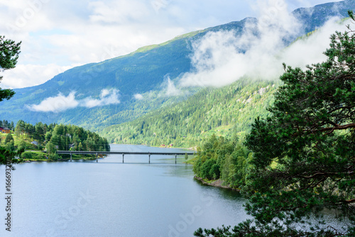 Bridge over fjord. Clouds sweep across the forest on the mountainside. Location Nore along route 40 in Norway.