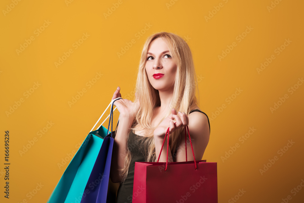 Young blondy girl holding shopping bags isolated over yellow background. Young blondy girl holding shopping bags isolated over yellow background.