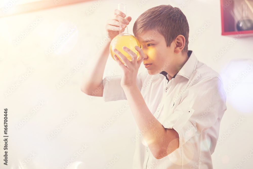 Serious boy holding bottle with yellow reagent Serious boy holding bottle with yellow reagent