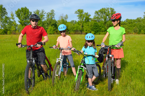 Family on bikes outdoors, happy active parents and two kids cycling outdoors on spring meadow, fitness and healthy lifestyle concept
