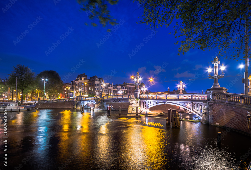 Fototapeta premium Amsterdam at night, with flowers and bicycles on the bridge, Holland, Netherlands.