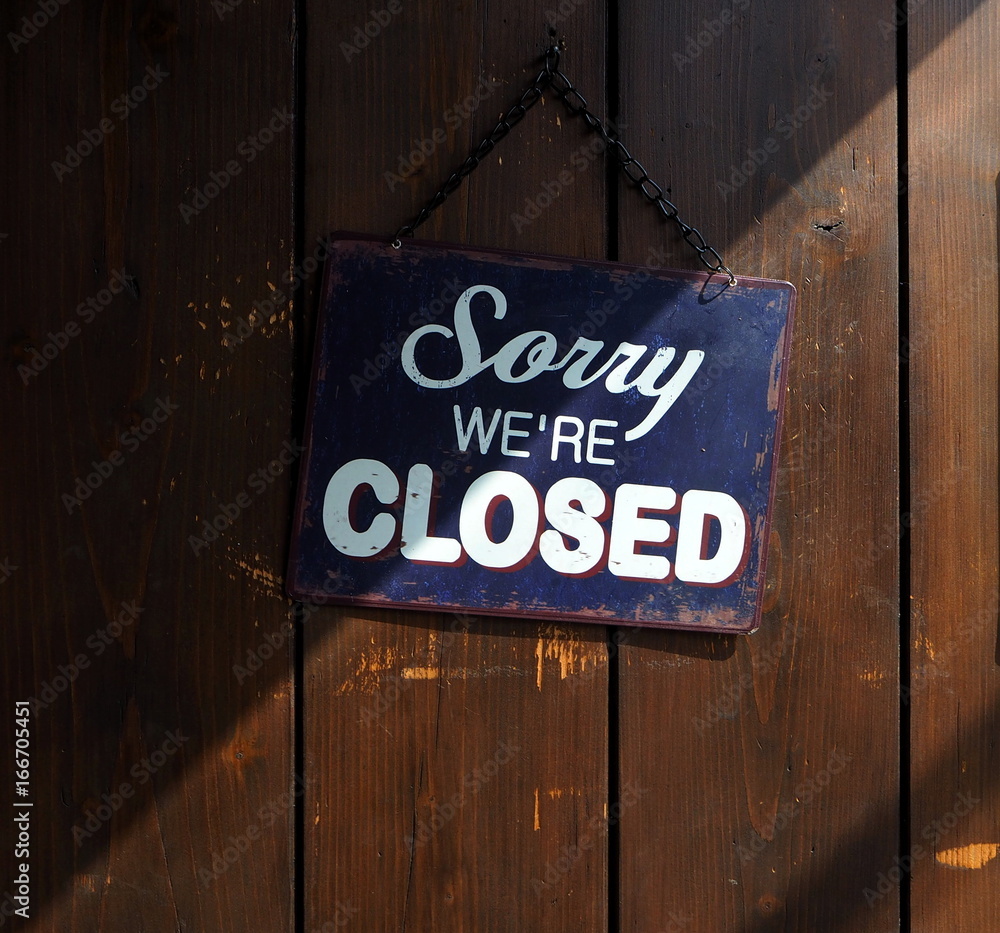  Sorry we're closed, blue and white retro sign on old wooden door, with a shadow that divides it into a clear and dark part