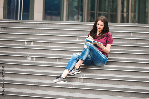Beautiful woman reading a book on the steps of the building. © nagaets