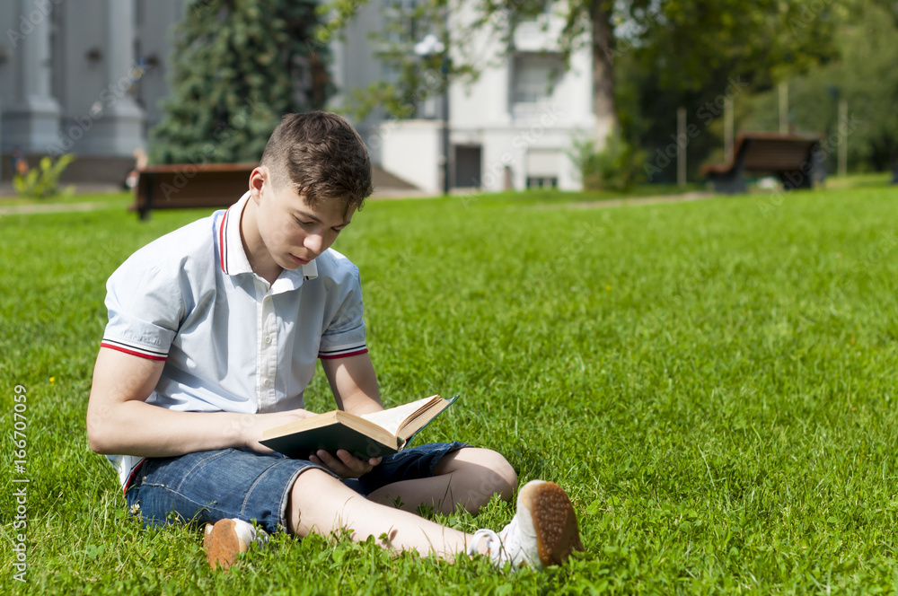 Young man reading a book sitting on the grass