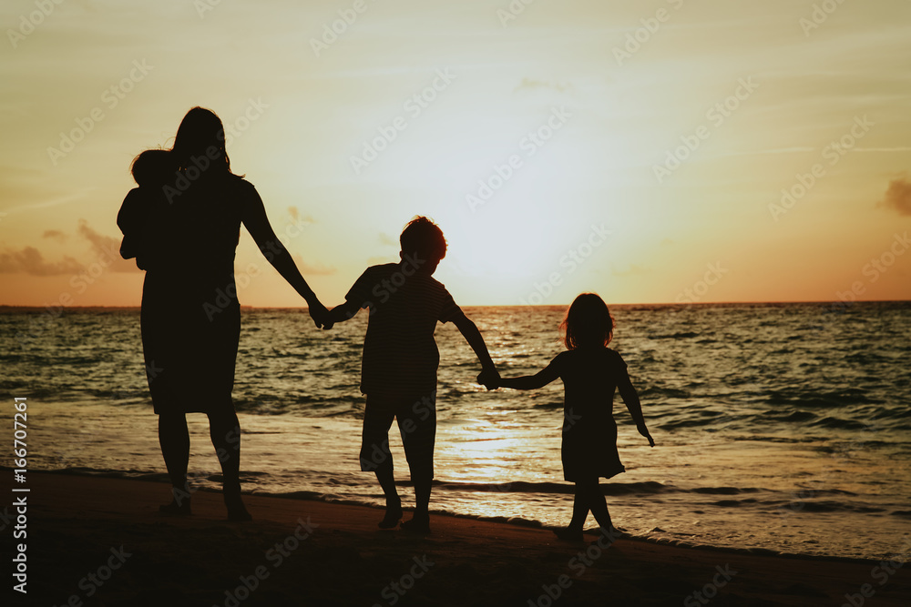 mother with three kids walking on beach at sunset