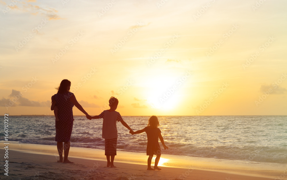 mother with three kids walking on beach at sunset
