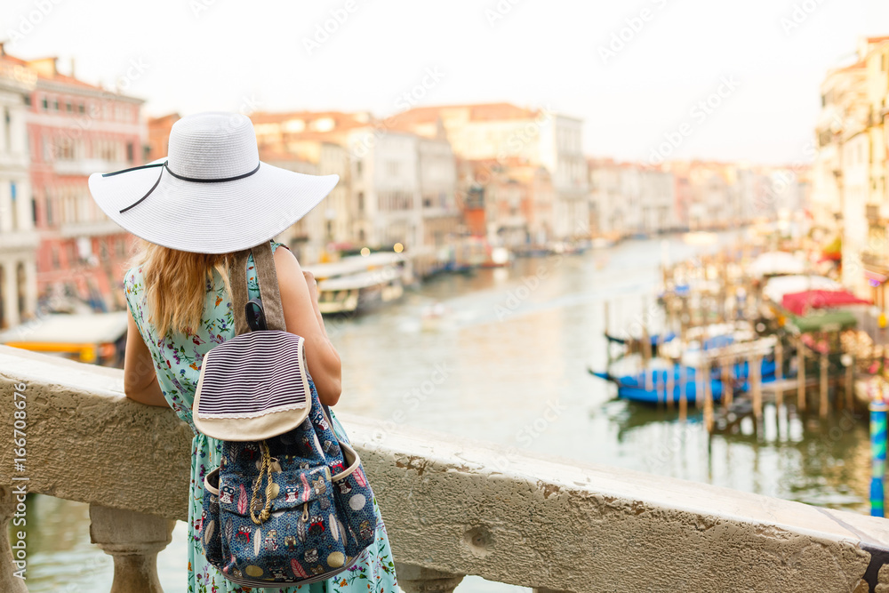 Woman in blue dress and hat walking in street in Venice, Italy cheerful and happy in rear view showing back of sundress.
