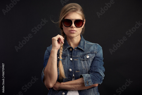 Stylish glamour woman wearing fashionable sunglasses and denim jacket on black background. 