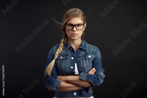 Serious female wearing stylish spectacles, posing in studio on black background. 