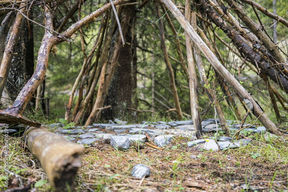 Obraz premium Stones arranged below a tent of branches arranged in a wigwam shape viewed low angle outdoors in a clearing in a forest