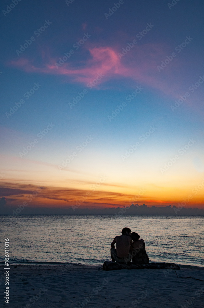 Couple sit together watching the sunset at Lankayan Island, Malaysia